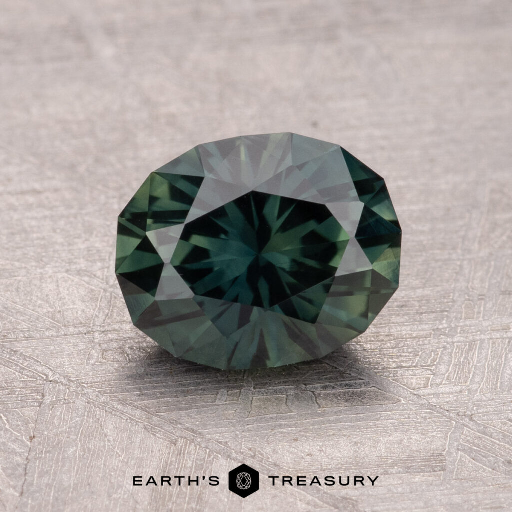 A round-cut, dark green 1.82-carat Australian Sapphire with intricate facets rests on a textured surface, with "Earth's Treasury" printed below.