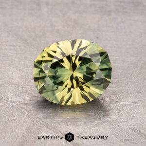 A 1.73-carat Australian sapphire, featuring a round faceted green-yellow surface, rests on a textured background with Earth's Treasury logo beneath.