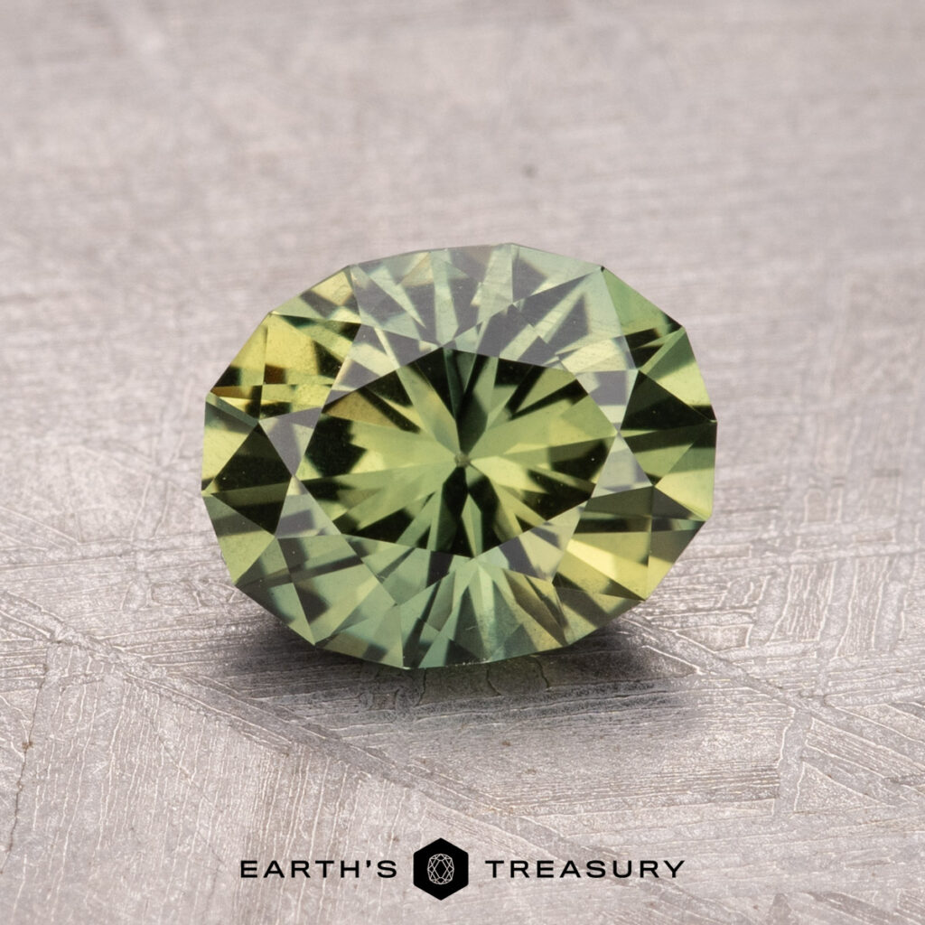 A 1.70-carat heated Australian sapphire gemstone, round and faceted in a vibrant green hue, rests atop a textured surface with the Earth’s Treasury logo below.