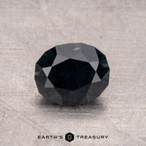 1.28-carat heated Australian Sapphire in dark teal hue on a textured surface.