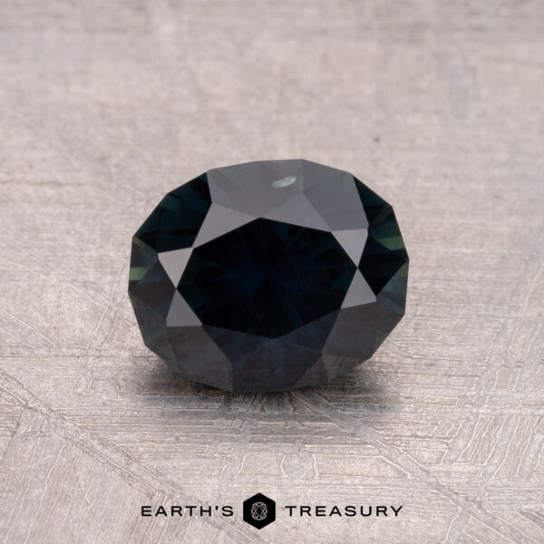 1.28-Carat Australian Sapphire (Heated) 1.28-carat heated Australian Sapphire in dark teal hue on a textured surface.
