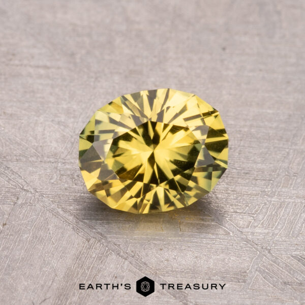 1.21-Carat Australian Sapphire (Heated) A 1.21-carat Australian Sapphire (Heated) gemstone, in a round cut with a yellow hue, rests on a textured gray surface with the text "Earth's Treasury" below.