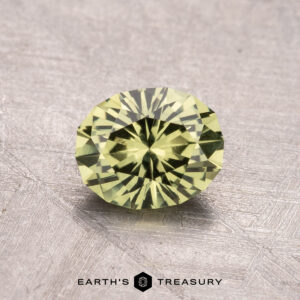 A round, faceted green gemstone measuring 1.09 carats rests on a textured surface with the "Earth's Treasury" logo below.