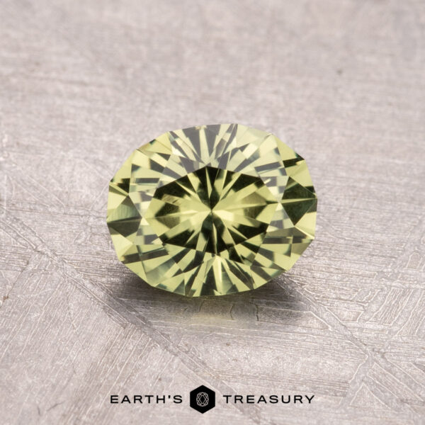 1.09-Carat Australian Sapphire (Heated) A round, faceted green gemstone measuring 1.09 carats rests on a textured surface with the "Earth's Treasury" logo below.