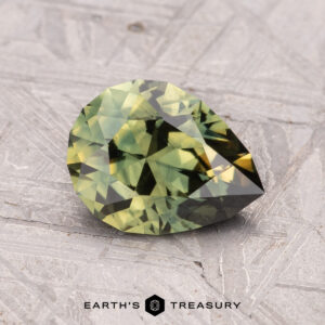 A 1.58-carat, faceted pear-shaped Australian sapphire (heated), resting on a textured gray surface.