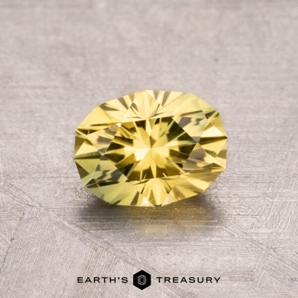 1.30-Carat Australian Sapphire (Heated) A 1.30-carat heated Australian sapphire, faceted and yellow, rests on a textured gray surface with the "Earth's Treasury" logo at the bottom.