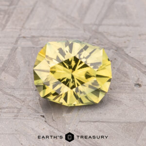 A faceted yellow gemstone rests on a textured gray surface with the label "1.57-Carat Australian Sapphire (Heated) - Earth's Treasury.