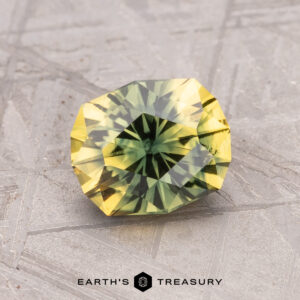 A faceted 1.56-carat Australian Sapphire (Heated), with green and yellow hues, rests on a textured surface.
