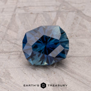 A 1.46-carat Australian sapphire gemstone, deep blue and heated, sits on a textured gray surface.
