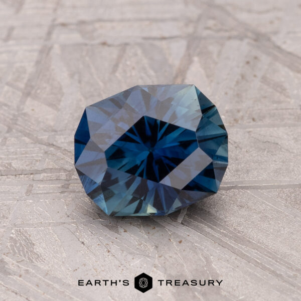 1.46-Carat Australian Sapphire (Heated) A 1.46-carat Australian sapphire gemstone, deep blue and heated, sits on a textured gray surface.