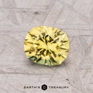 A 1.18-carat heated Australian sapphire with intricate facets is displayed against a textured gray surface.