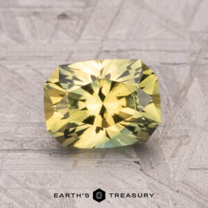 A 1.84-carat Australian Sapphire (heated), sparkling with a rectangular green-yellow faceted surface, rests on a textured gray background.