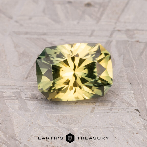 1.35-Carat Australian Sapphire (Heated) A rectangular, faceted yellow-green gemstone, the 1.35-Carat Australian Sapphire (Heated), is displayed on a textured surface with the "Earth's Treasury" logo beneath it.
