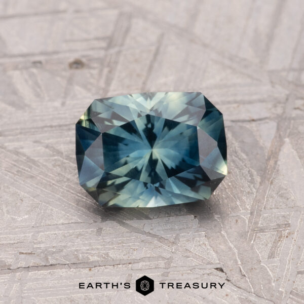 1.19-Carat Australian Sapphire (Heated) A 1.19-carat Australian Sapphire (heated) with a rectangular, faceted form and blue-green hues sits on a textured surface.