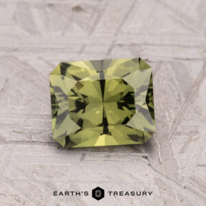 A faceted rectangular Australian Sapphire (1.62-Carat, Heated) in green rests on a textured gray surface, with the "Earth's Treasury" logo and text below.