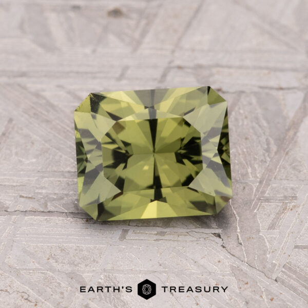 1.62-Carat Australian Sapphire (Heated) A faceted rectangular Australian Sapphire (1.62-Carat, Heated) in green rests on a textured gray surface, with the "Earth's Treasury" logo and text below.