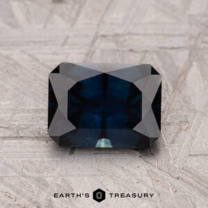 A 1.59-carat Australian Sapphire (heated), rectangular with faceted edges, rests on a textured gray surface.