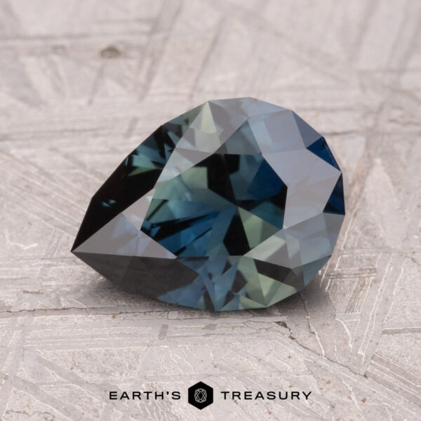 2.06-Carat Australian Sapphire (Heated) A faceted, dark teal 2.06-Carat Australian Sapphire (Heated) gemstone on a textured surface with "Earth's Treasury" visible at the bottom.