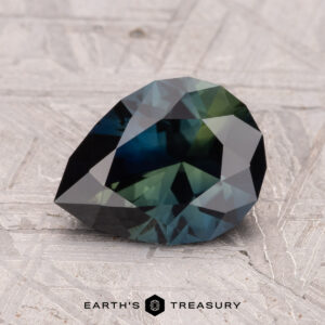 A 2.06-carat faceted, pear-shaped Australian Sapphire with dark green and blue hues is placed on a textured surface. The "Earth's Treasury" logo is visible at the bottom.