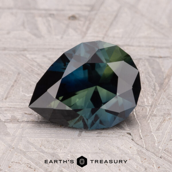 2.06-Carat Australian Sapphire (Heated) A 2.06-carat faceted, pear-shaped Australian Sapphire with dark green and blue hues is placed on a textured surface. The "Earth's Treasury" logo is visible at the bottom.