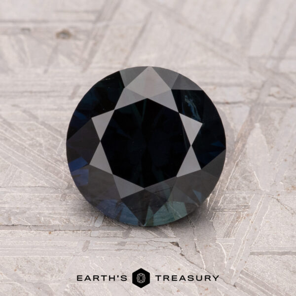 1.91-Carat Australian Sapphire (Heated) A 1.91-carat Australian sapphire, heated and dark blue with geometric facets, rests on a textured light gray surface. The "Earth's Treasury" logo is at the bottom.