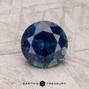 A 1.76-carat Australian sapphire (heated) with a faceted cut rests on a textured surface.