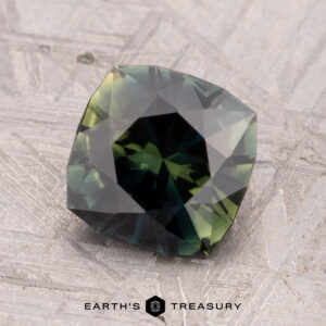 A 2.12-carat heated Australian sapphire with a faceted square shape and checkerboard pattern set on a textured gray surface.