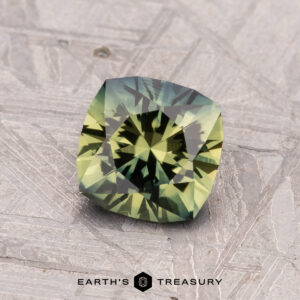 A 1.23-carat Australian sapphire (heated), showcasing green and yellow facets, rests on a textured gray surface.