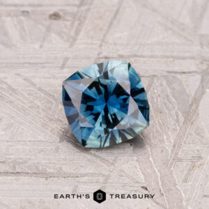 A 0.64-carat Australian sapphire (heated) in a cushion cut rests on a textured surface, with the "Earth's Treasury" logo beneath.