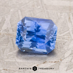A 2.17-carat Cornflower Blue Ceylon Sapphire with an octagonal shape is displayed on a textured beige surface, with the Earth’s Treasury logo visible below.