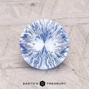 A 2.00-carat round brilliant-cut Ceylon sapphire on a textured surface, with text below reading "EARTH'S TREASURY.
