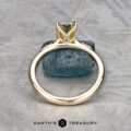 The "Kyria" ring in 14k yellow gold with a 1.41-carat Montana sapphire stands upright on a rough blue stone atop a textured gray surface, with "EARTH'S TREASURY" shown at the bottom.