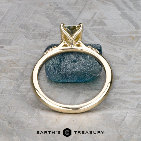 The "Kyria" ring in 14k yellow gold with 1.41-carat Montana sapphire The "Kyria" ring in 14k yellow gold with a 1.41-carat Montana sapphire stands upright on a rough blue stone atop a textured gray surface, with "EARTH'S TREASURY" shown at the bottom.