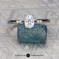 The "Kyria" ring in platinum, featuring a 0.80-carat Montana sapphire, is displayed on a rough blue crystal atop a patterned gray surface, with the "Earth's Treasury" logo below.