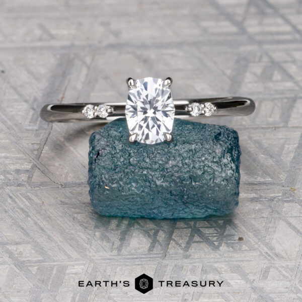 The "Kyria" ring in platinum with 0.80-carat Montana sapphire The "Kyria" ring in platinum, featuring a 0.80-carat Montana sapphire, is displayed on a rough blue crystal atop a patterned gray surface, with the "Earth's Treasury" logo below.