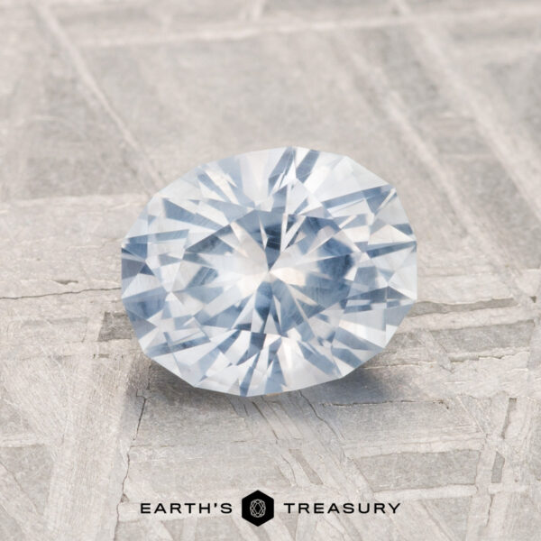 1.35-Carat Montana Sapphire A round, faceted 1.35-Carat Montana Sapphire is displayed on a textured gray surface with the "Earth's Treasury" logo at the bottom.