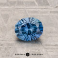 The 1.02-Carat Montana Sapphire, round and faceted, is shown on a textured gray surface with "EARTH'S TREASURY" printed below.