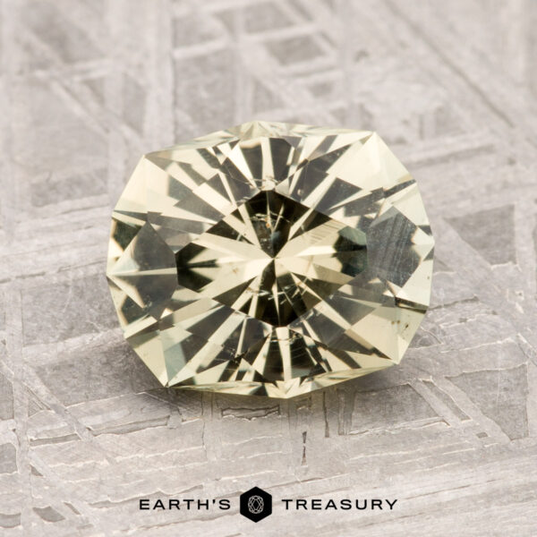 2.05-Carat Montana Sapphire A 2.05-carat Montana Sapphire with a round, faceted cut and light yellow hue rests on a textured gray surface, with the "Earth's Treasury" logo visible below.