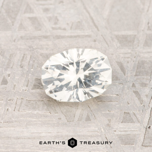 0.81-Carat Montana Sapphire The 0.81-Carat Montana Sapphire, a faceted near colorless gemstone, is shown on a textured geometric surface with "EARTH'S TREASURY" displayed at the bottom.