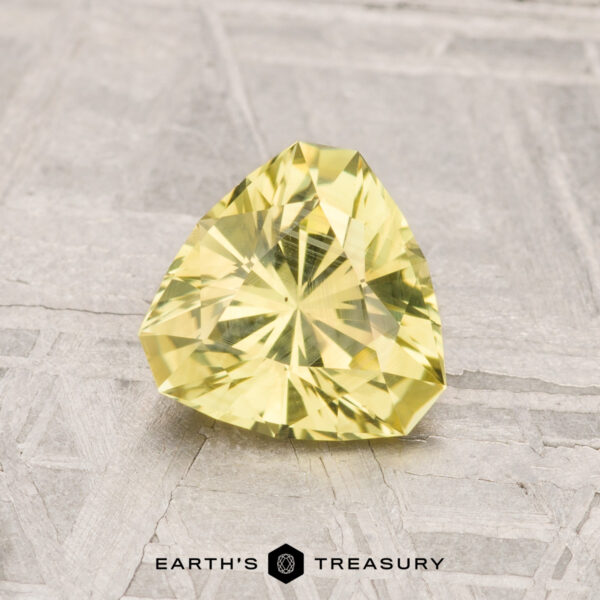 1.19-Carat Montana Sapphire A 1.19-carat Montana Sapphire, trillion-cut and yellow, is displayed on a textured surface with "Earth's Treasury" text at the bottom.