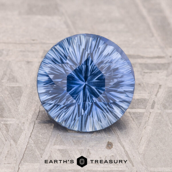 2.10-Carat Ceylon Sapphire (Heated) A round blue 2.10-carat Ceylon sapphire with a starburst pattern sits on a textured gray surface. "Earth's Treasury" logo at the bottom.