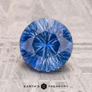 A 2.16-carat Ceylon Sapphire (heated) with intricate internal facets rests on a textured surface, adorned with the "Earth's Treasury" logo at the bottom.