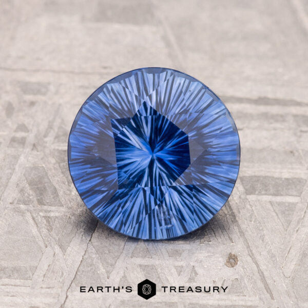 1.84-Carat Ceylon Sapphire (Heated) A 1.84-carat, brilliantly cut round Ceylon sapphire with intricate patterns is placed on a textured gray surface. "Earth's Treasury" is visible at the bottom.
