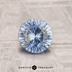 A 1.04-carat heated Ceylon sapphire with a blue starburst pattern rests on a textured surface. Text reads "Earth's Treasury.