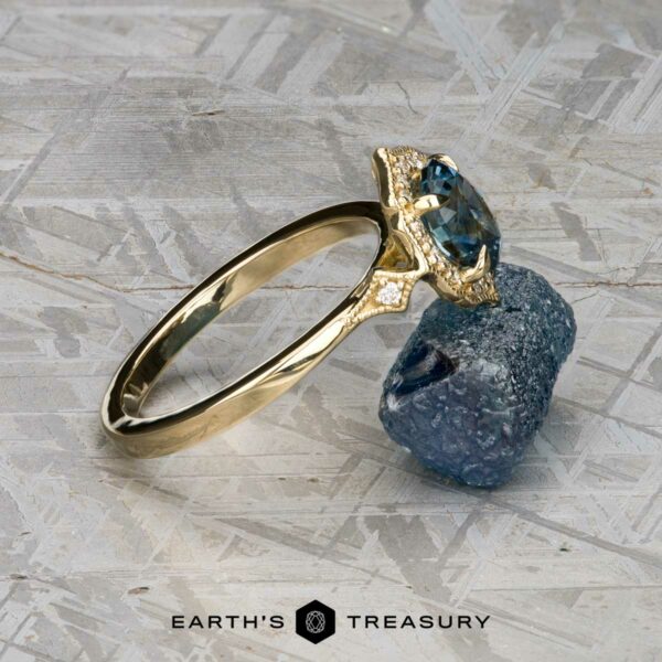The "Ailette" ring in 14K yellow gold with 1.44-carat Montana sapphire The "Ailette" ring in 14K yellow gold, featuring a 1.44-carat Montana sapphire and accent stones, rests on a rough blue mineral atop a textured surface. The text "Earth's Treasury" appears below.