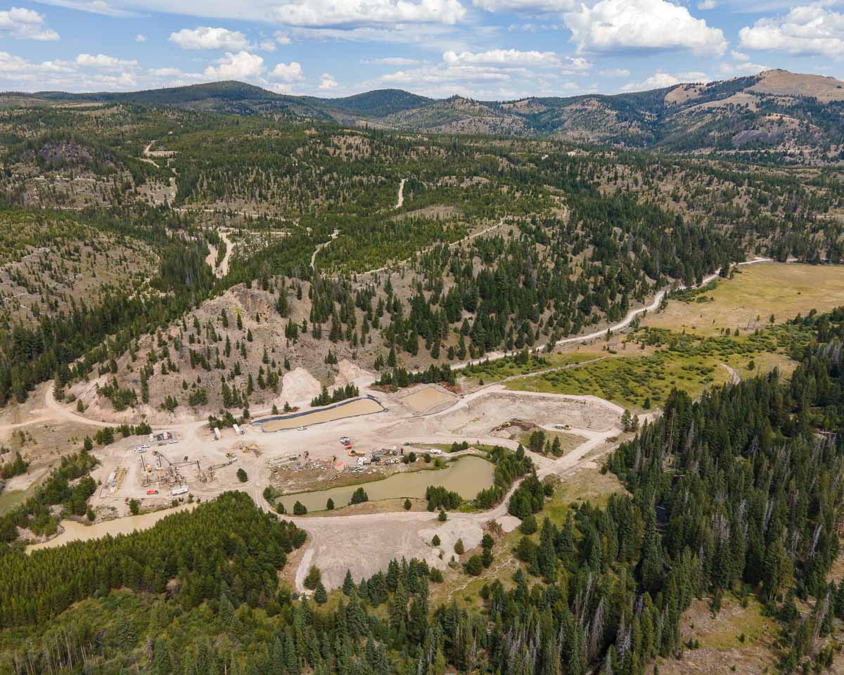 The "Mining Landscape Perspective" captures an aerial view of a mountainous terrain with a large dirt excavation site, enveloped by dense forest and winding roads, beneath a partly cloudy sky.