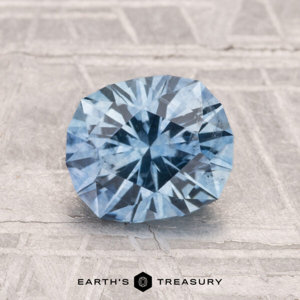 1.93-Carat Montana Sapphire (Heated) A round, faceted 1.93-carat heated Montana sapphire is showcased on a textured gray surface with "EARTH'S TREASURY" displayed at the bottom.