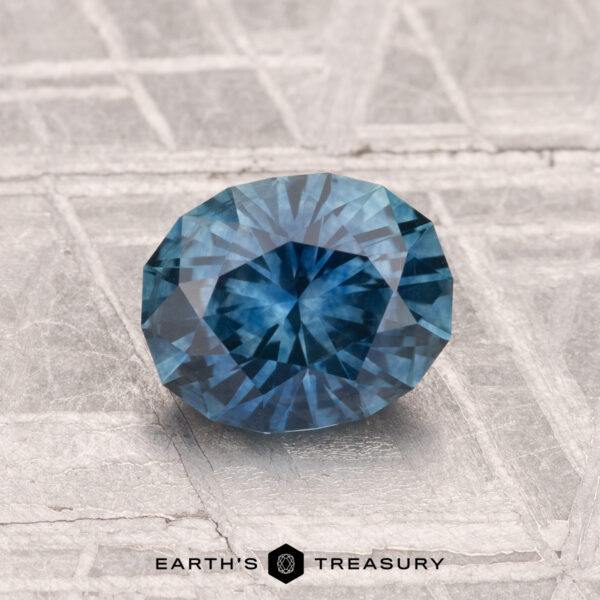 1.30-Carat Montana Sapphire (Heated) A 1.30-carat heated Montana sapphire is displayed on a textured, metallic surface with "EARTH'S TREASURY" at the bottom.
