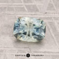 A 1.71-carat heated Montana sapphire with a rectangular faceted cut and pale blue-green hue rests on a textured gray surface displaying the "Earth's Treasury" logo at the bottom.