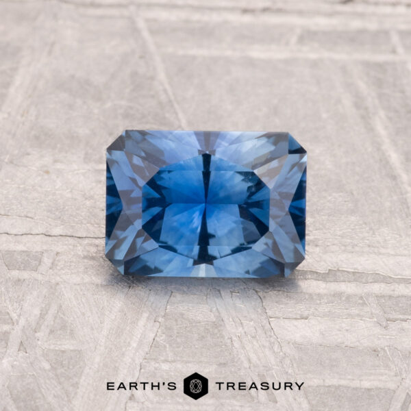 1.10-Carat Montana Sapphire (Heated) A 1.10-carat Montana sapphire (heated) with faceted edges is displayed on a textured light gray surface, featuring the text "EARTH'S TREASURY" at the bottom.